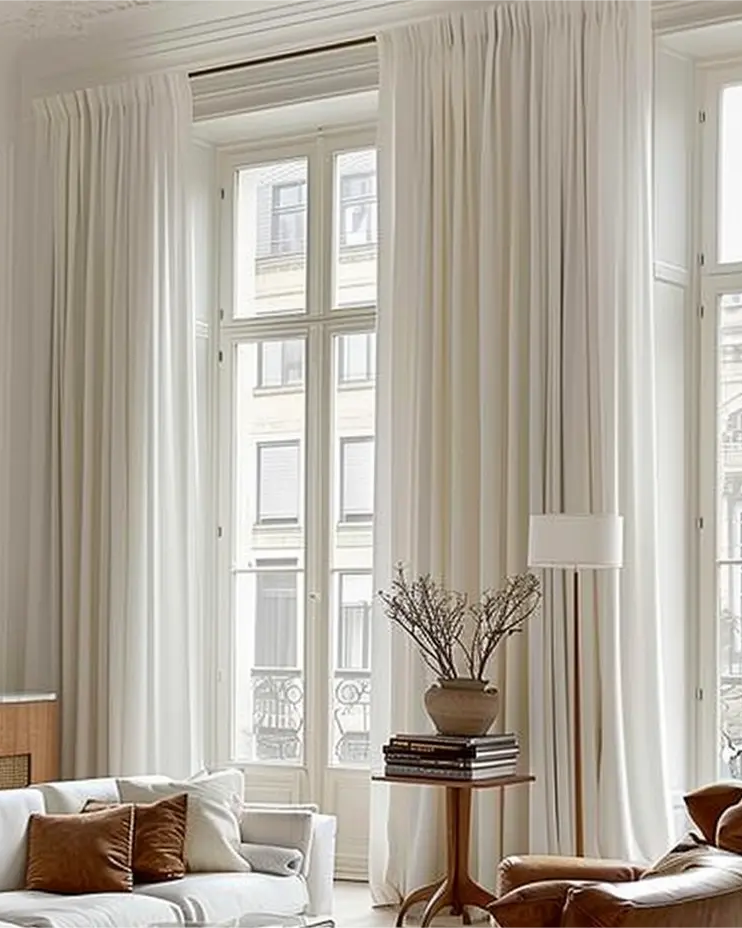 Luxurious living room with floor-to-ceiling white curtains, large windows, and modern furniture, featuring a cozy seating area.