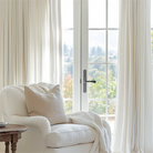 The living room is adorned with white linen grommet curtains draped over rods.