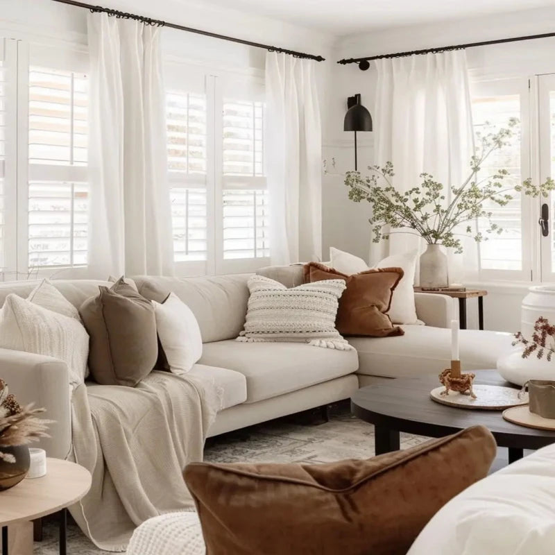 Cozy living room with white drapery, neutral-toned pillows, and warm decor accents creating an inviting atmosphere