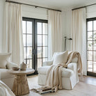 White linen pleated curtains are installed on black rods in the living room.