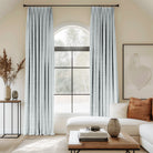 Living room with arched window and light blue velvet pleated curtains.