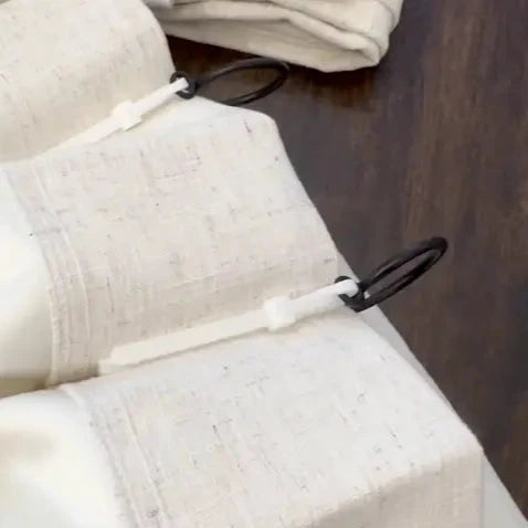 Close-up of pleated linen curtains with black curtain rings and hooks, highlighting textured fabric and modern hanging style.