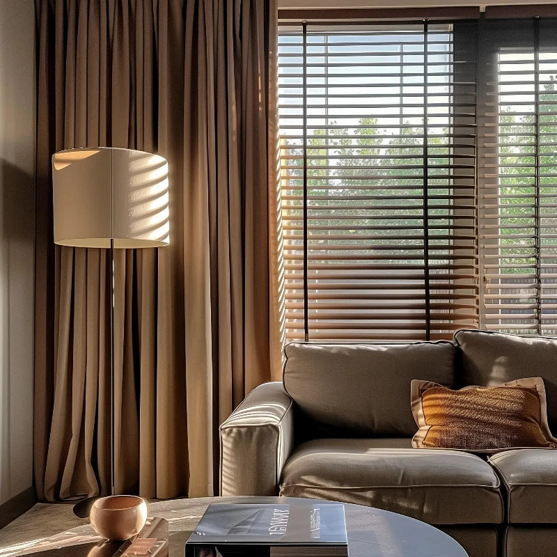 Modern living room with warm drapery, sleek furniture, and natural light filtering through blinds, creating a cozy ambiance.